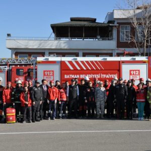 Group of firefighters and officials posing in front of a red Batman Fire Department truck on a sunny day.