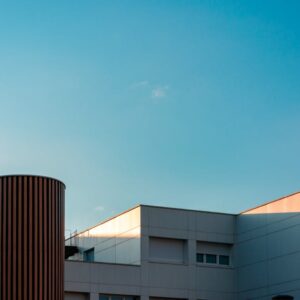 Modern white building with a tall cylindrical brown vent against a clear blue sky, early evening light casting warm highlights on the roof edges.