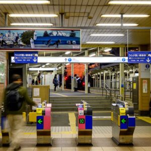 Busy train station entrance with automatic ticket gates and a blurred traveler walking past.
